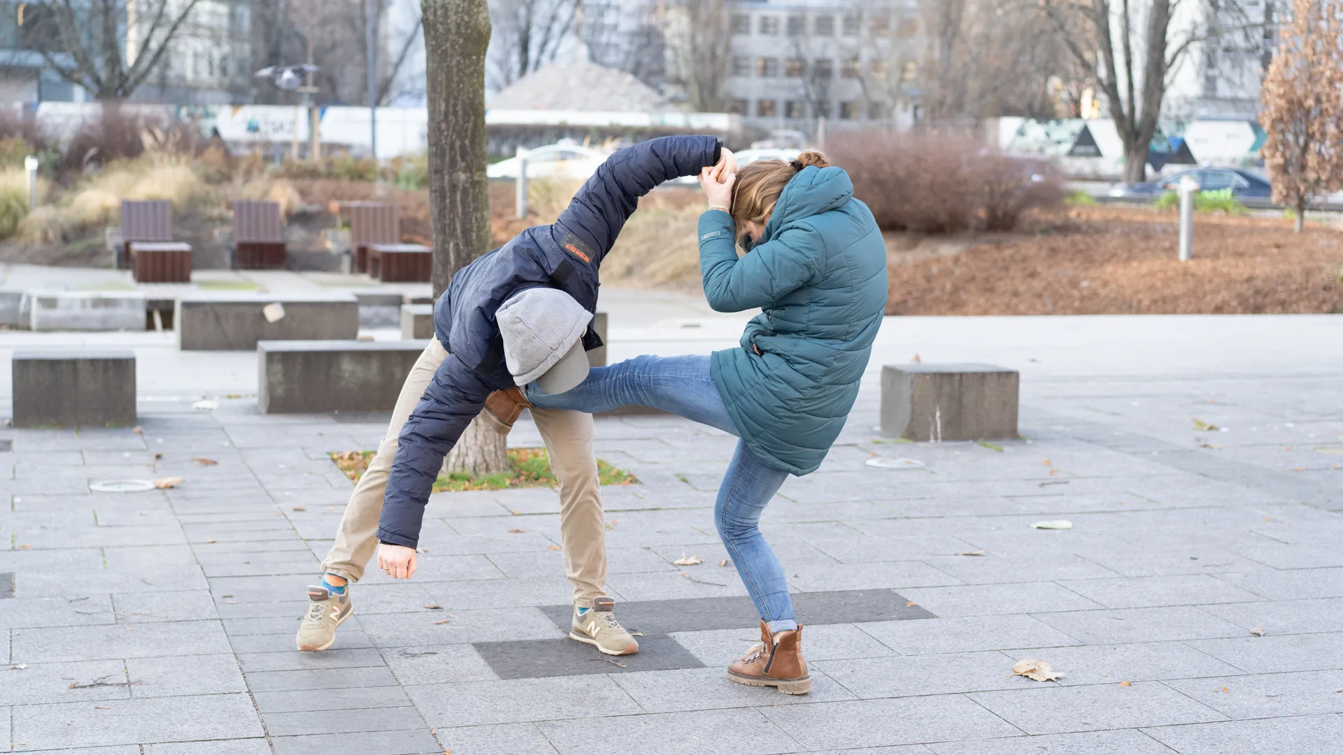 A woman driving a front-kick into a padded attacker during a self-defence drill